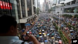 抗议者戴着口罩和打着雨伞游行在香港的一条街道上,一名男子在拍照。2019年10月6日， 美联社照片