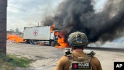 A police officer looks at a burning Red Cross vehicle that was destroyed in a Russian strike in the Donetsk region, Sept. 12, 2024. (Police of the Donetsk Region via AP)