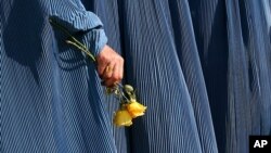 An Afghan woman holds flowers during a fair to mark Women's Day in Kabul, Afghanistan, March 8, 2007. At the time, roughly two out of five Afghan marriages were forced, and 45 percent of women are married by the age of 18. According to UNIFEM, at least on