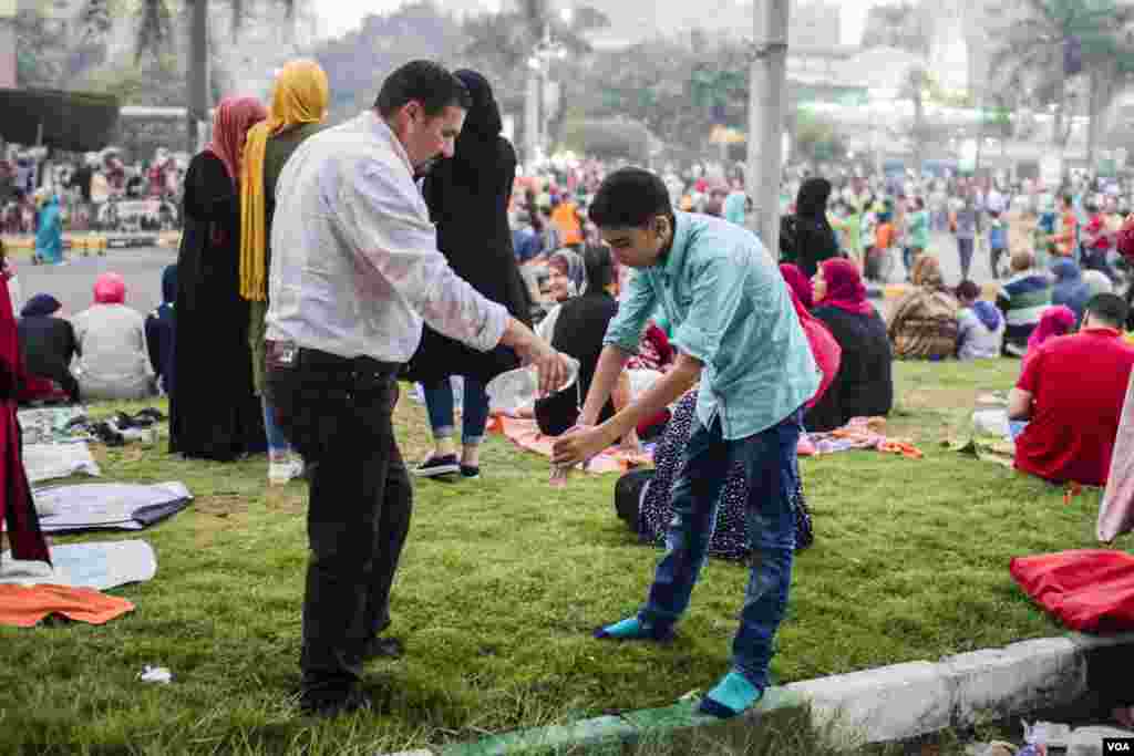 Seorang ayah membantu anaknya berwudhu sebelum sholat Idul Fitri di lapangan Mostafa Mahmoud di Kairo, Mesir, 25 Juni 2017. (H. Elrasam/VOA)