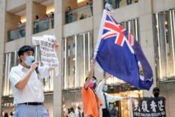 A pro-democracy demonstrator wearing a face mask waves the British colonial Hong Kong flag as another one holds a sign during a protest against new national security legislation in Hong Kong, China, June 1, 2020.