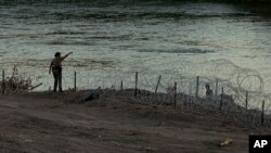 ARCHIVO - Un soldado de Texas habla con los migrantes mientras estos caminan a lo largo de alambre de púas y tratan de cruzar la frontera hacia EEUU, el 6 de julio de 2023. Los migrantes en el bus trataban de alcanzar el límite entre EEUU y México. 