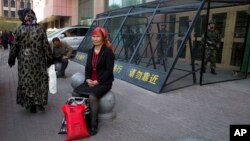 FILE - An Uighur woman rests near a cage protecting heavily armed Chinese paramilitary policemen on duty in Urumqi in China's northwestern region of Xinjiang, May 1, 2014. Uighur homeland has been blanketed with stifling surveillance, from armed checkpoin