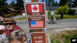 A family visits across the U.S.-Canada border at the Peace Arch Historical State Park as a cyclist rides past on the Canadian side, Aug. 9, 2021, in Blaine, Wash.