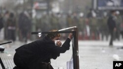 A woman takes cover during clashes after the start of a national strike in Santiago, Chile, August 24, 2011