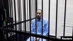 FILE - Saadi Gadhafi, son of Moammar Gadhafi, sits behind bars during a hearing at a courtroom in Tripoli, Libya, Feb. 7, 2016.