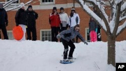 Sekelompok orang dewasa dan anak-anak menikmati olah raga papan seluncur salju di sore hari, di bukit dekat kampus Universitas Wake Forest, di Winston-Salem, North Carolina, 17 Januari 2018. 