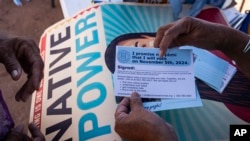 FILE - Local organizer Maria Calamity instructs a resident on how to properly fill out a pledge card promising to vote in the upcoming presidential election, on the Navajo Nation in Ganado, Arizona, Oct. 11, 2024.