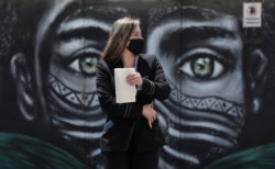 A woman wearing a face mask amid the spread of the new coronavirus walks past a mural of an Indigenous man in Bogota, Colombia, July 3, 2020.