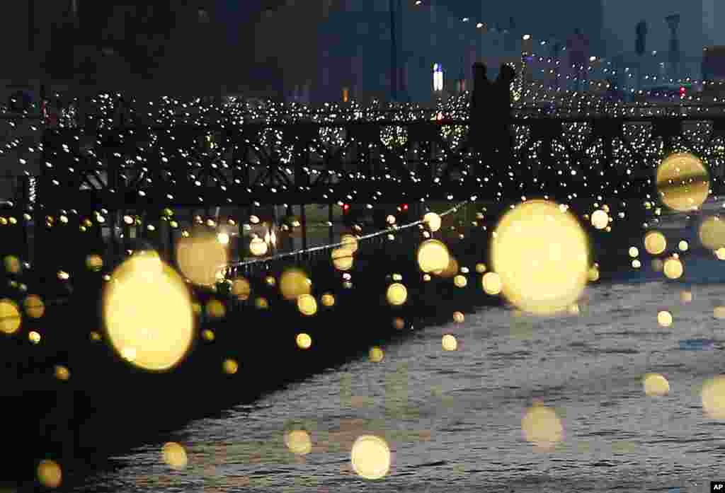 People walk on a bridge as Christmas lights illuminate the Darsena dei Navigli, the neighborhood named for the canals that run through this area of Milan, Italy.