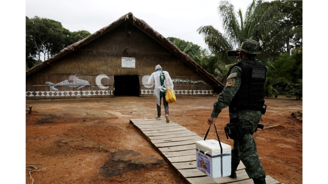 FILE - A municipal health worker and an environmental military police officer carry the AstraZeneca/Oxford vaccine as they enter an Indigenous hut at the Tupe Sustainable Development Reserve in Manaus, Brazil, Feb. 9, 2021.