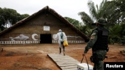 Seorang petugas kesehatan dan polisi membawa vaksin COVID-19 AstraZeneca / Oxford memasuki gubuk tradisional di Cagar Pembangunan Berkelanjutan Tupe, tepi sungai Negro di Manaus, Brazil, 9 Februari 2021.
