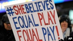 FILE - A girl holds up a sign for equal pay for the U.S. women soccer players, April 4, 2017, during the first half of an international friendly soccer match between the United States and Colombia, in East Hartford, Conn. 