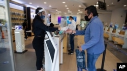 A mobile phone store employee wearing a mask and face shield to curb the spread of the new coronavirus tends to a client at a shop in the Polanco neighborhood of Mexico City, Thursday, July 30, 2020. Mexico's economic activity plummeted 18.9% in the…