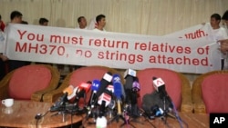 Chinese relatives of passengers on board the missing Malaysia Airlines flight MH370 hold a sign as they speak to reporters at a hotel in Subang Jaya, Malaysia, March 30, 2014.