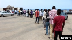 FILE - Migrants queue to receive food aid distributed by UNHCR amid the coronavirus pandemic, in Tripoli, Libya, May 12, 2020. The IOM has repatriated more than 100 Ghanaian migrants due to the ongoing conflict and virus spread in Libya. 