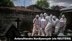 Petugas Pemkot mengenakan alat pelindung diri (APD) membawa peti jenazah korban COVID-19 di pemakaman umum, Badran, Yogyakarta, 22 Juni 2021. (Foto: Antara/Hendra Nurdiyansyah via Reuters)