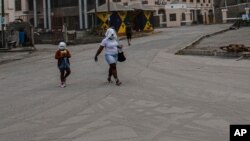 A woman and a girl walk wearing protective head coverings walk on a street covered with volcanic ash a day after the La Soufriere volcano erupted, in Kingstown, on the eastern Caribbean island of St. Vincent, April 10, 2021.