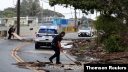 Police officers and a bystander use plywood boards to push beach debris off the road in Kaaawa, Hawaii, July 26, 2020, ahead of Hurricane Douglas, which is causing ocean swells in certain areas around Oahu with water washing up on some roads.