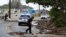 Police officers and a bystander use plywood boards to push beach debris off the road in Kaaawa, Hawaii, July 26, 2020, ahead of Hurricane Douglas, which is causing ocean swells in certain areas around Oahu with water washing up on some roads.