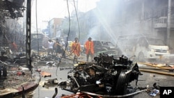 Thai fire fighters walk near a wreckage of a car while others trying to put off fire at a building after the car bomb blasted in Yala, southern Thailand, March 31, 2012. 