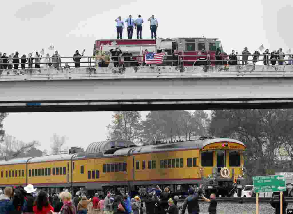 Firefighters stand on their truck and salute along with other attendants on an overpass as the train carrying the body of former president George H.W. Bush travels past on the way to Bush's final internment Thursday, Dec. 6, 2018, in Spring, Texas.