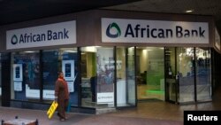 FILE - A cleaner walks past a branch of African Bank in Cape Town.