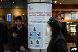 FILE - A woman wearing a face mask passes a Public Health England sign, warning arriving passengers that the coronavirus has been detected in Wuhan in China, at Terminal 4 of London Heathrow Airport in west London on Jan. 28, 2020.