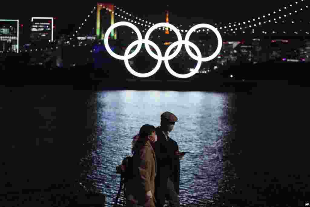 A man and a woman walk past near the Olympic rings floating in the water in the Odaiba section in Tokyo, Japan.