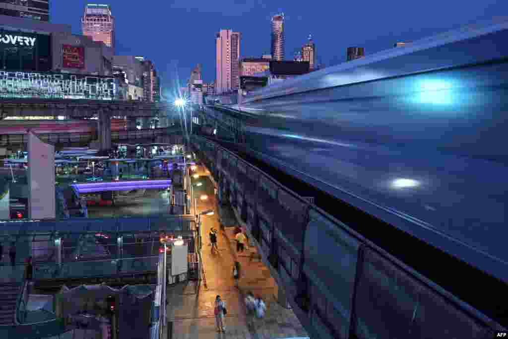 Pedestrians use the skywalk bridge between shopping malls as BTS trains pass above them in Bangkok, Thailand.