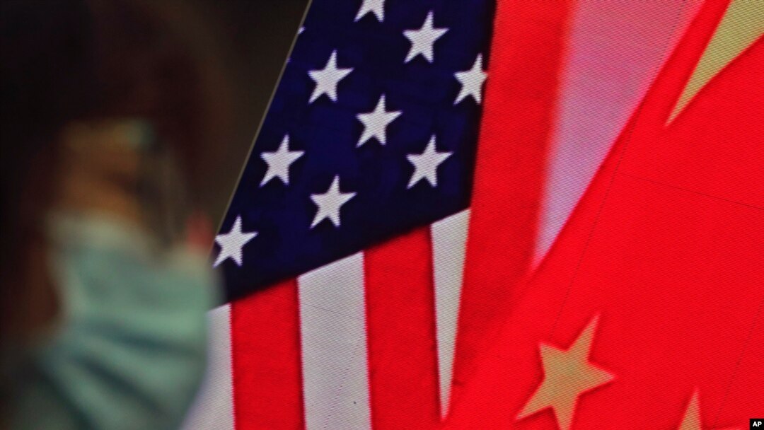 Seorang perempuan mengenakan masker duduk dekat layar yang menampilkan gambar bendera China dan AS di Forum Lanting mengenai hubungan AS-China, di Beijing, 22 Februari 2021.