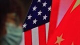 A woman wearing a face mask sits near a screen showing China and U.S. flags as she listens to a speech by Chinese Foreign Minister Wang Yi at the Lanting Forum on bringing China-U.S. relations, Beijing, Feb. 22, 2021.