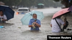 Residents wade through floodwaters on a flooded road amid heavy rainfall in Zhengzhou, Henan province, China, July 21, 2021.