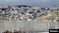 FILE - A car drives along a road near the Israeli barrier in the Palestinian town of Abu Dis in the West Bank, as Jerusalem is seen in the background, Feb. 15, 2017.
