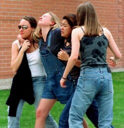 FILE - Unidentified young women head to a library near Columbine High School where students and faculty members were evacuated after two gunmen went on a shooting rampage in the school, in Colorado, April 20, 1999.