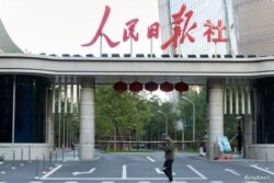 Un hombre con un teléfono inteligente camina frente a la sede del periódico oficial de China, People´s Daily.