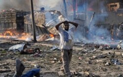 FILE - A man walks past a body and destroyed buildings at the scene of a blast in the capital Mogadishu, Somalia, Oct 14, 2017.