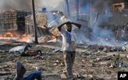 FILE - A man walks past a body and destroyed buildings at the scene of a blast in the capital Mogadishu, Somalia, Oct 14, 2017.