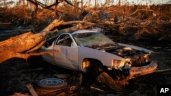 FILE - A car sits crushed by a fallen tree from a tornado as the sun rises in Beauregard, Ala., March 6, 2019. Storms on March 9 caused damage in Arkansas and Mississippi.