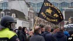 Riots police separate pro and anti immigration demonstrators as a man waves a flag reading "Islamists Not Welcome" during a Pegida demonstration in Amsterdam, Netherlands, Feb. 6, 2016. 