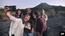 Wisatawan domestik berswafoto dengan latar belakang Gunung Merapi, Yogyakarta, 6 Agustus 2019. (Foto: AP)