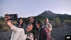 Sejumlah wisatawan domestik berswafoto dengan latar belakang Gunung Merapi, Yogyakarta, 6 Agustus 2019. (Foto: Slamet Riyadi/AP)