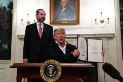 FILE - Secretary of Health and Human Services Alex Azar looks on as President Donald Trump shows a spending bill to combat the coronavirus, at the White House, March 6, 2020, in Washington.