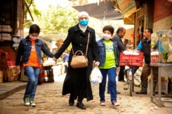 In this photo released on April 18, 2020, by the Syrian official news agency SANA, shows a Syrian woman with her sons wearing masks due to the coronavirus, as they walk on a street in Damascus, Syria.