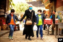 In this photo released on April 18, 2020, by the Syrian official news agency SANA, shows a Syrian woman with her sons wearing masks due to the coronavirus, as they walk on a street in Damascus, Syria.