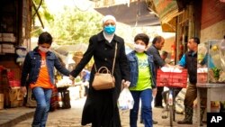 FILE - In this photo released April 18, 2020, by the Syrian official news agency SANA, a Syrian woman and her sons wear masks to protect against the coronavirus as they walk on a street in Damascus.