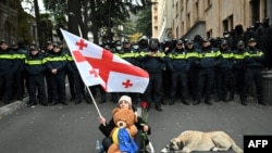 A woman holds a red rose and a Georgian flag as she faces law enforcement officers during a protest against the results of the last month&#39;s parliamentary elections in Tbilisi as the Parliament convene its first session. (Photo by Vano SHLAMOV / AFP)