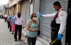 FILE - A security guard takes a woman's temperature as a precaution against the new coronavirus, as she lines up to enter a bank in Tegucigalpa, Honduras, June 18, 2020.