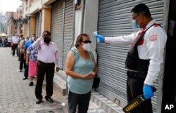 FILE - A security guard takes a woman's temperature as a precaution against the new coronavirus, as she lines up to enter a bank in Tegucigalpa, Honduras, June 18, 2020.