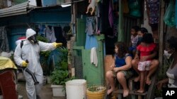 A worker gestures to residents as he sprays disinfectant in an alley to help contain the spread of the coronavirus, at the Santa Marta slum in Rio de Janeiro, Brazil, April 10, 2020.